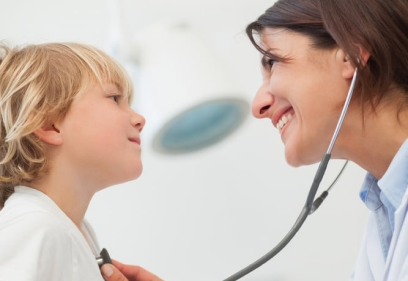 Smiling doctor auscultating a child with a stethoscope in examination room